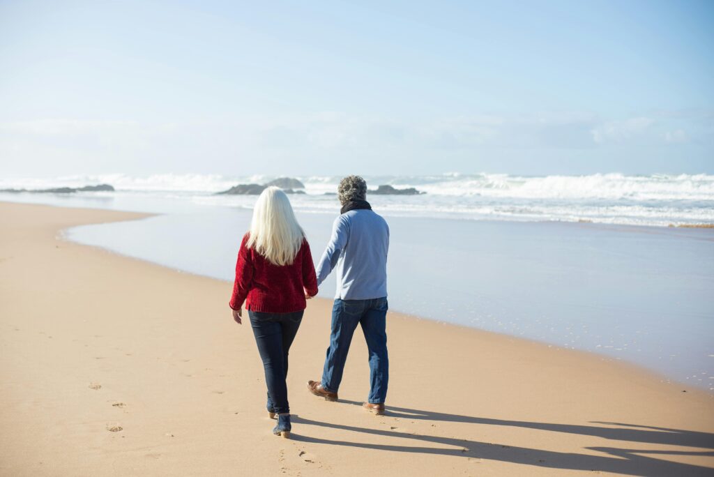 A couple walks hand in hand on a sandy beach with the ocean waves gently crashing nearby in Portugal.