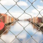 A heart-shaped padlock adorns a metal fence overlooking Trondheim's scenic riverfront.