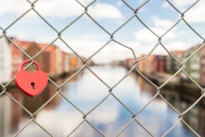 A heart-shaped padlock adorns a metal fence overlooking Trondheim's scenic riverfront.