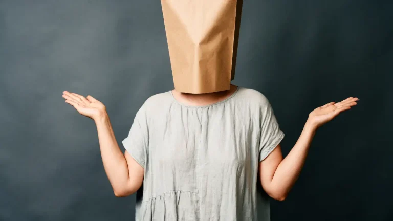 vrouw met een papieren zak over haar hoofd en haar handen omhoog in een vragende houding