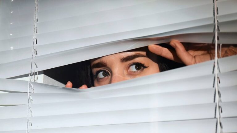 nieuwsgierige vrouw die achter de gordijnen vandaan gluurt